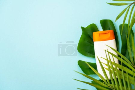Téléchargez les photos : Produits solaires sur fond bleu avec des feuilles de palmier. Protection solaire pour les vacances d'été, détente à la plage et bains de soleil. Pose plate avec espace pour le texte. - en image libre de droit
