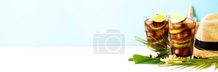 Photo for Cuba Libre iced drink, alcoholic with palm leaves and sea shells. Long banner format. - Royalty Free Image