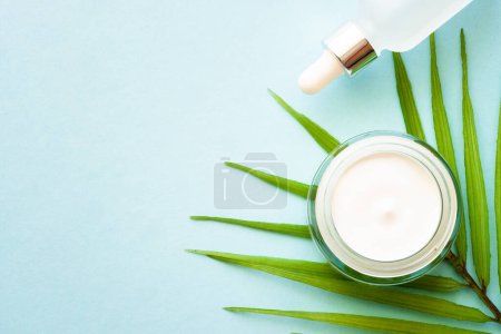 Photo for Cream jar and serum bottle with palm leaf on blue background. Natural cosmetic concept. Flat lay with copy space. - Royalty Free Image