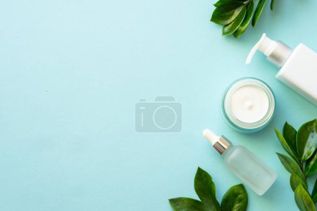 Téléchargez les photos : Produits cosmétiques naturels plat posé sur le bleu. Crème et sérum aux feuilles vertes. - en image libre de droit