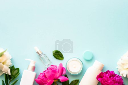 Foto de Productos cosméticos naturales. Crema, suero, tónico con hojas verdes y flores. Piso sobre fondo azul. - Imagen libre de derechos