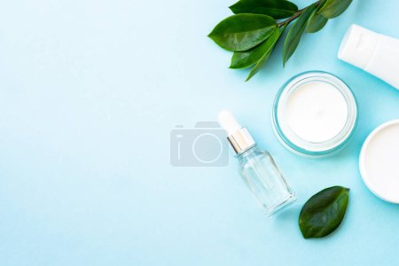 Photo for Natural cosmetic, cream jar with green leaves on blue. Flat lay with copy space. - Royalty Free Image