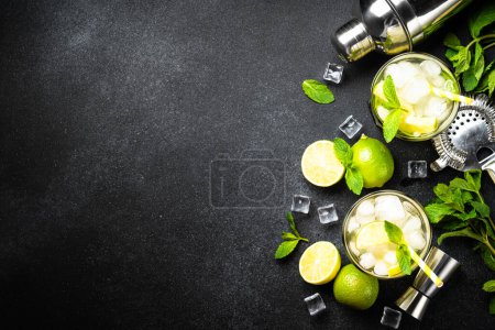 Téléchargez les photos : Mojito au rhum, citron vert, menthe et glace sur fond noir avec ustensiles de bar. Pose plate avec espace de copie. - en image libre de droit