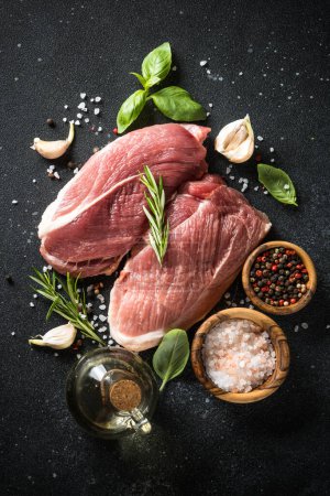 Photo for Raw meat steaks with spices, herbs and oil at dark background. Top view, vertical. - Royalty Free Image