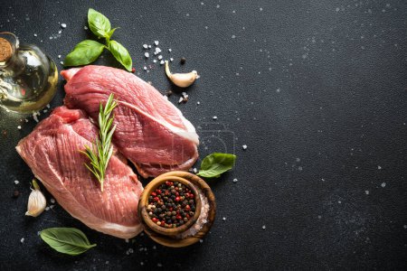 Photo for Raw meat steaks with spices, herbs and oil at dark background. Top view with space for text. - Royalty Free Image
