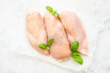 Foto de Filete de pollo, pechuga de carne de pollo cruda con albahaca fresca en fondo blanco. Vista superior. - Imagen libre de derechos