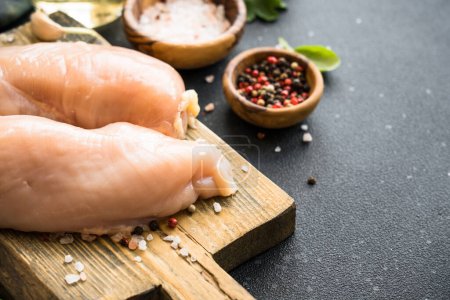 Photo for Chicken fillet, raw chicken meat breast with spices on wooden board at dark background. - Royalty Free Image