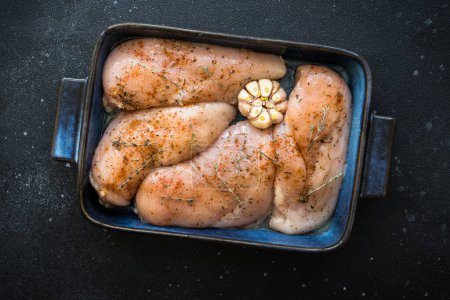 Foto de Filete de pollo, pechuga de carne de pollo cruda con especias y ajo en la sartén. Vista superior. - Imagen libre de derechos