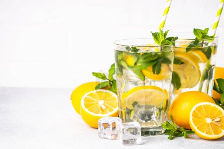 Téléchargez les photos : Citronnade en verre sur table blanche avec citrons frais et menthe. Boisson froide d'été. - en image libre de droit