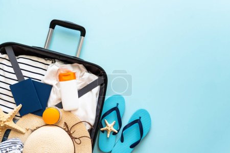 Photo for Open Suitcase with summer cloth, hat, passports and flip flops on blue background. Happy Holidays, travel concept. Flat lay image. - Royalty Free Image