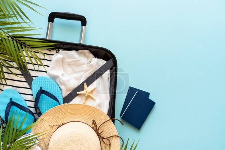 Open Suitcase with summer cloth, shoes and accessories on blue background. Summer Holidays, travel concept. Flat lay image.
