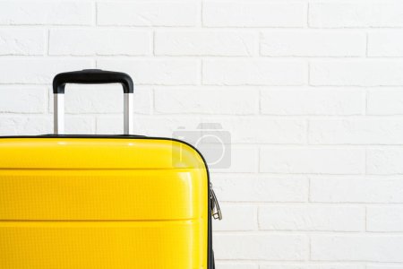 Foto de Maleta de equipaje amarilla cerca de la pared de ladrillo blanco en el estudio. - Imagen libre de derechos
