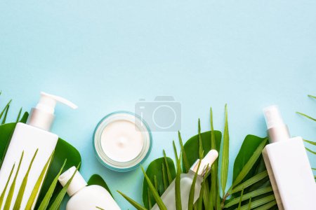 Téléchargez les photos : Cosmétique d'été, ensemble de produits cosmétiques avec des feuilles de palmier sur bleu. Vue supérieure avec espace de copie. - en image libre de droit
