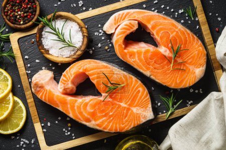 Photo for Salmon steaks on cutting board at black background. Top view with ingredients for cooking. - Royalty Free Image