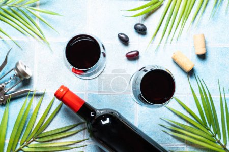Téléchargez les photos : Vin rouge sur fond bleu. Vin en verre avec raisin, bouteille de vin et feuilles de palmier. Image de pose plate avec espace de copie. - en image libre de droit