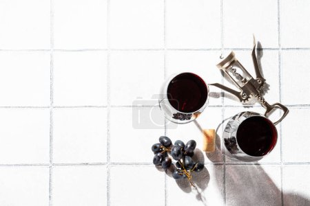Téléchargez les photos : Verre à vin sur fond blanc. Deux verres avec raisin et tire-bouchon avec des ombres dures. - en image libre de droit
