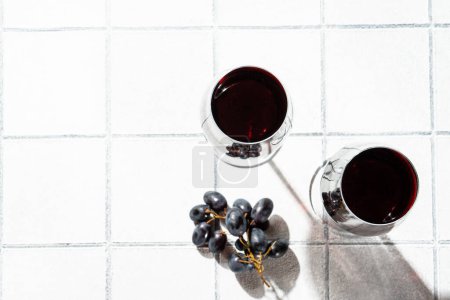 Téléchargez les photos : Vin rouge sur fond blanc. Deux verres au vin, raisin aux ombres dures. - en image libre de droit