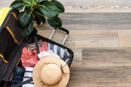 Photo for Open Suitcase with summer cloth, hat and passports. Travel concept, packing baggage. Flat lay image on wooden background. - Royalty Free Image