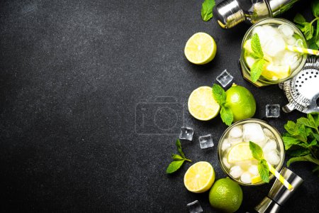 Téléchargez les photos : Mojito au rhum, citron vert, menthe et glace sur fond noir avec ustensiles de bar. Pose plate avec espace de copie. - en image libre de droit