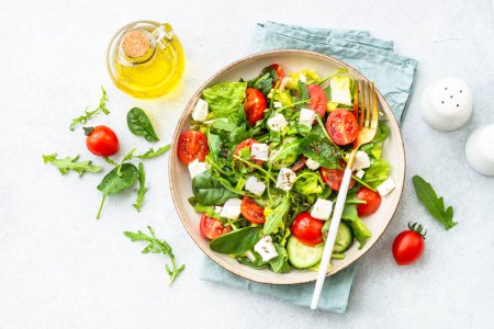 Foto de Ensalada verde con espinacas, rúcula y tomates con aceite de oliva. Vista superior en blanco. - Imagen libre de derechos