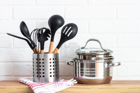 Foto de Kitchen table, kitchen utensils, cooking pots with wooden cutting board, white modern interior. - Imagen libre de derechos