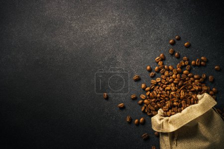 Foto de Granos de café tostados en bolsa de arpillera en fondo negro.. Vista superior con espacio para copiar - Imagen libre de derechos