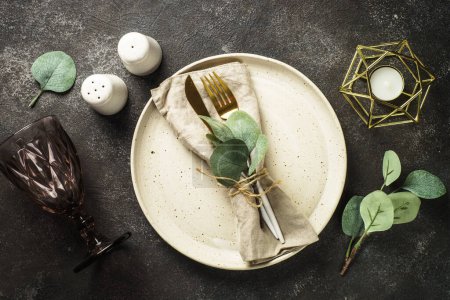 Foto de Table setting with white craft plate, cutlery and decorations at black stone table. Top view image. - Imagen libre de derechos
