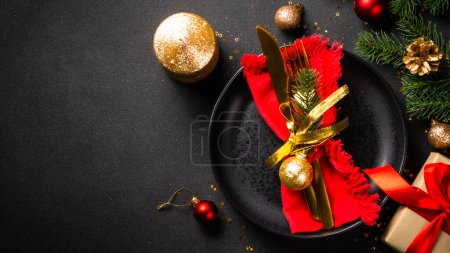Photo for Christmas table with black plate, golden cutlery and holiday decorations. Top view on black. - Royalty Free Image