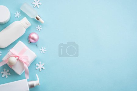 Téléchargez les photos : Cosmétique naturelle d'hiver avec des décorations de vacances et boîte cadeau sur fond bleu. Concept de scincare d'hiver. Image de pose plate. - en image libre de droit