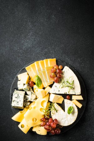 Téléchargez les photos : Assiette au fromage avec assortiment de fromages artisanaux et raisin sur fond noir. Vue supérieure avec espace de copie. - en image libre de droit