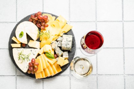 Photo for Cheese platter with craft cheese assortment on slate board at white tile background. Top view. - Royalty Free Image