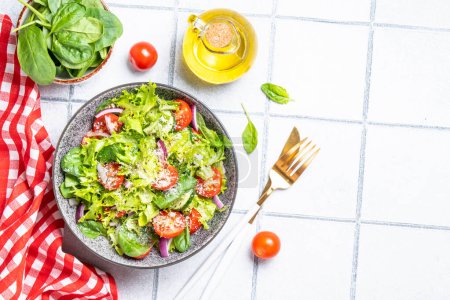 Téléchargez les photos : Salade de légumes verts aux feuilles fraîches. Vue de dessus sur fond de tuiles blanches. - en image libre de droit