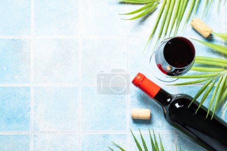 Photo for Red wine on blue background. Glass wine with grape, wine bottle and palm leaves. Flat lay image with copy space. - Royalty Free Image
