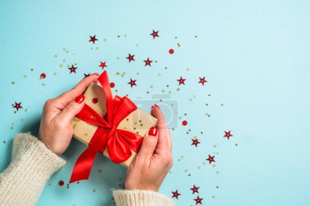 Photo for Christmas present box with red ribbon. Woman is giving a present. Flat lay image on blue with copy space. - Royalty Free Image