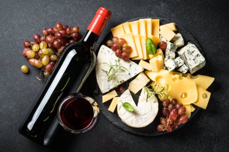 Téléchargez les photos : Assiette au fromage avec assortiment de fromages artisanaux sur ardoise et vin rouge sur fond noir. Vue du dessus. - en image libre de droit
