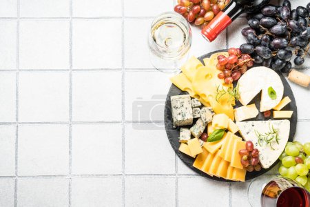 Photo for Cheese platter with craft cheese assortment on slate board at white tile background. Top view. - Royalty Free Image
