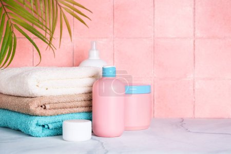 Téléchargez les photos : Serviettes propres et produits cosmétiques dans la salle de bain en couleurs roses. - en image libre de droit