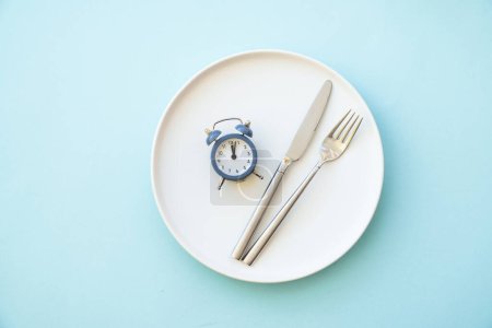 Concepto de ayuno intermitente. Alimentación saludable, dieta. Placa blanca con cubiertos y reloj.