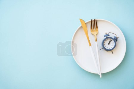Concepto de ayuno intermitente. Alimentación saludable, dieta. Placa blanca con cubiertos y reloj.