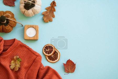 Téléchargez les photos : Pull chaud, feuilles d'automne, bougie et décor sur fond bleu. Image de pose plate avec espace de copie. - en image libre de droit