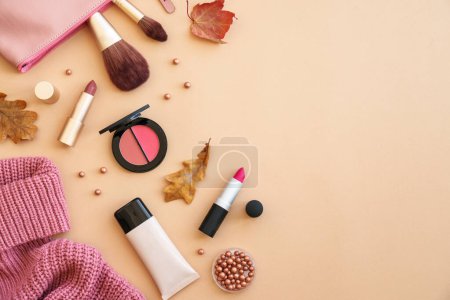 Photo for Cosmetic products with Cloth and accessories at autumn background. Sweater, cosmetic bag and make-up products with autumn leaves. Flat lay with copy space. - Royalty Free Image