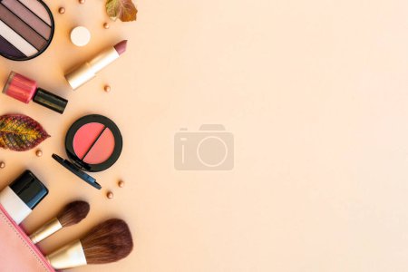 Foto de Maquillaje productos de belleza en fondo pastel con decoraciones de otoño. Polvo, cimentación, rímel, lápiz labial. Asiento plano con espacio para texto. - Imagen libre de derechos