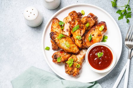 Téléchargez les photos : Ailes de poulet grillées avec sauce dans une assiette artisanale à table blanche. Vue du dessus. - en image libre de droit