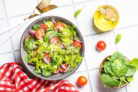 Téléchargez les photos : Salade de légumes verts aux feuilles fraîches. Aliments sains, menu diététique. Vue de dessus sur fond de tuiles blanches. - en image libre de droit