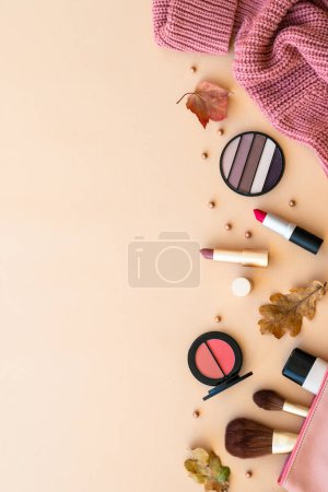 Foto de Fondo de belleza de otoño. Productos de maquillaje, suéter de punto y hojas de otoño al fondo pastel. Puesta plana. - Imagen libre de derechos