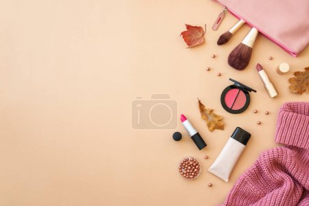 Téléchargez les photos : Tissu et accessoires sur fond de couleur. Pull, sac cosmétique et produits de maquillage avec feuilles d'automne. Image à plat avec espace pour le texte. - en image libre de droit