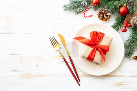 Photo for Christmas table setting with holiday decorations. White plate with present box and cutlery. Flat lay with copy space. - Royalty Free Image