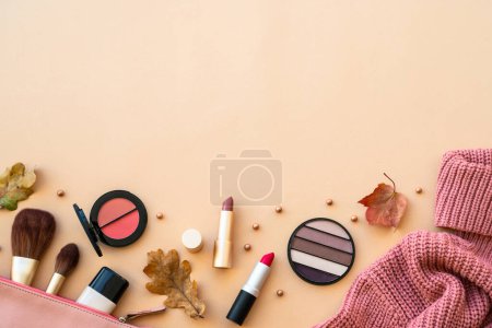 Foto de Fondo de belleza de otoño. Productos de maquillaje, suéter de punto y hojas de otoño al fondo pastel. Puesta plana. - Imagen libre de derechos