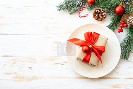 Téléchargez les photos : Cadre de table de Noël avec décorations de vacances. Assiette blanche avec boîte cadeau et couverts. Pose plate avec espace de copie. - en image libre de droit