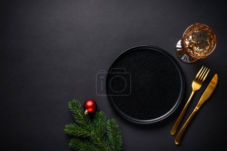 Photo for Christmas table setting with black plate, wine glass, golden cutlery and holidays decorations. Flat lay with space for text. - Royalty Free Image